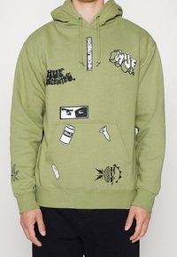 Felpa verde oliva realizzata in tessuto morbido, con diverse stampe grafiche, tra cui occhi, loghi e motivi, dotata di una tasca a marsupio nella parte anteriore.