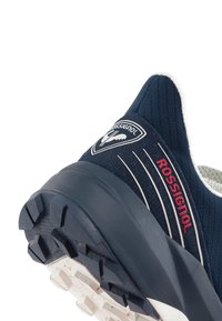 Tmavě modrá sportovní bota s textilním svrškem, bílými akcenty, logem a texturovanou gumovou podrážkou s výraznými drážkami.