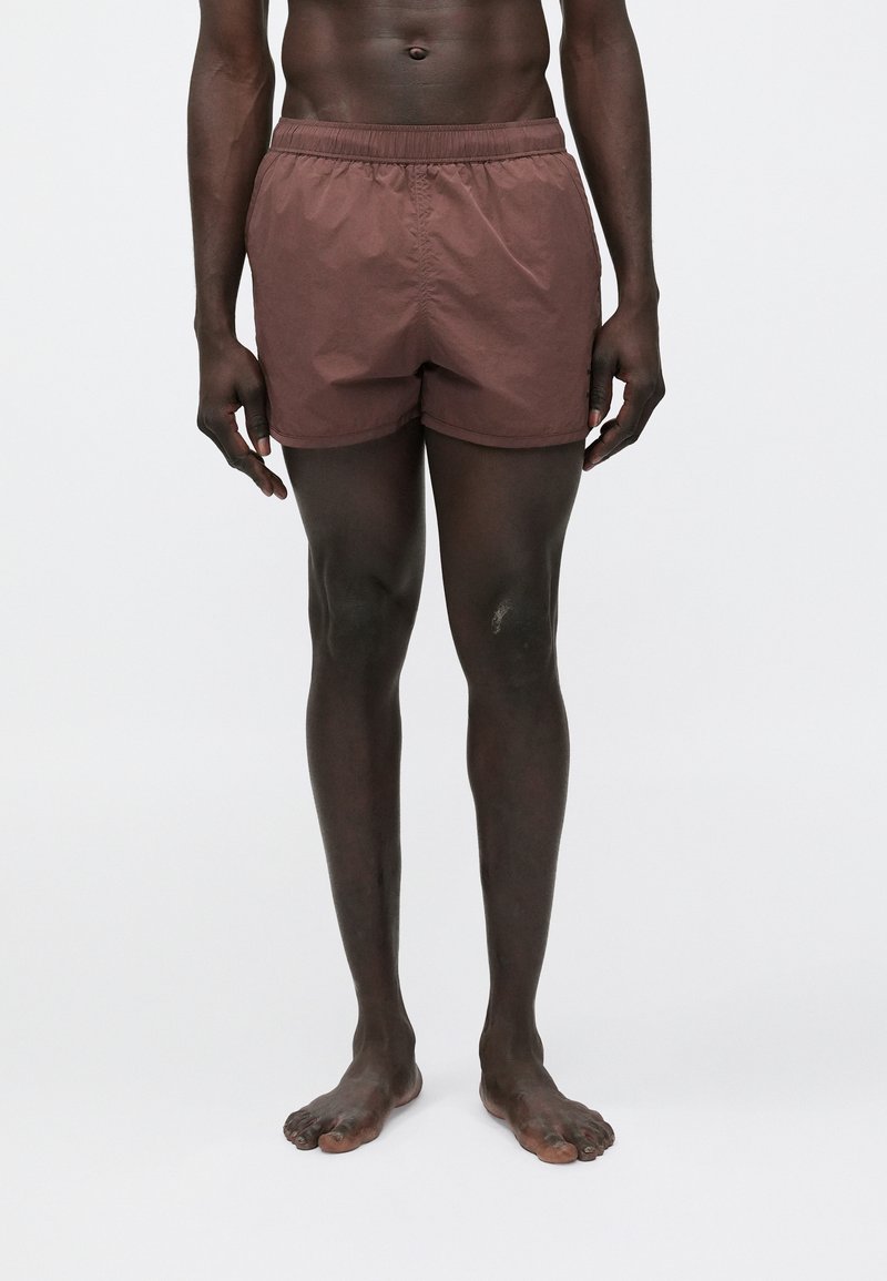 Brązowe spodenki kąpielowe z elastycznym pasem, lekką tkaniną i luźnym krojem. Charakteryzują się jednolitym kolorem bez widocznych wzorów ani elementów metalowych.