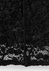 Černá květinová krajka s texturovaným povrchem a složitými vzory. Má centrální šev a jemné, delikátní zakončení.