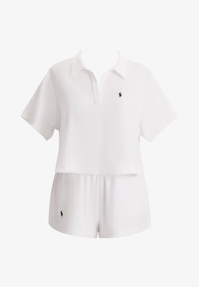 Λευκό πόλο τοπ με κοντά μανίκια και V-λαιμόκοψη, συνδυασμένο με σορτς στο ίδιο χρώμα. Διαθέτει μικρό μαύρο λογότυπο στο στήθος και στα σορτς. Μαλακή υφή.