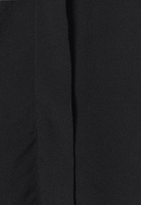 Detailní záběr na černou texturovanou tkaninu s vertikálním švem vedoucím středem.