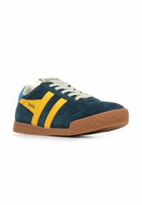 Zapatillas de ante en azul oscuro con rayas amarillas, suela de goma con patrón texturizado y cordones beige. Logo de la marca en el lateral y en la lengüeta.