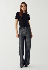 Crna prilagođena majica s kratkim rukavima u kombinaciji s hlačama visokog struka, širim nogavicama od metalik teksturiranog sivog materijala, koje imaju dizajn s pet džepova i kopčanje na gumb.