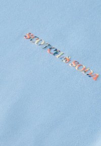 Tessuto azzurro chiaro con una superficie testurizzata, caratterizzato da un logo in rilievo multicolore che recita "SCOTCH & SODA" al centro.