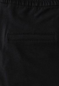 Zwarte stof met een gladde textuur, voorzien van een gestikte achterzak en een elastische tailleband. Ideaal voor casual kleding of comfort.