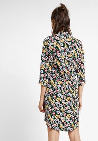 Vestito floreale su sfondo nero, caratterizzato da vivaci fiori gialli, rosa e viola. Maniche lunghe, vita fasciata, orlo fino al ginocchio.