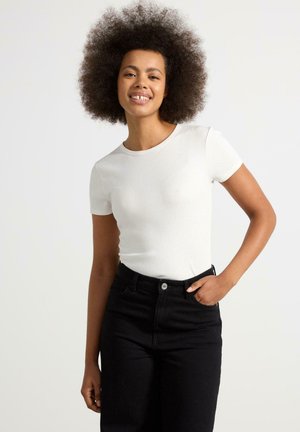 Vit ribbad kortärmad topp med rund halsringning, tillsammans med högmidjade svarta jeans. Enkel, figurnära design med en slät yta.