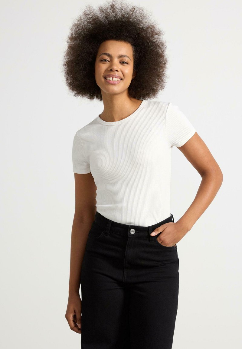 Vit ribbad kortärmad topp med rund halsringning, tillsammans med högmidjade svarta jeans. Enkel, figurnära design med en slät yta.
