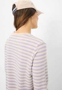 Baumwolloberteil mit vertikalen Streifen in Lavendel und Creme. Rundhalsausschnitt mit einer strukturierten Oberfläche, ergänzt durch eine beigefarbene Mütze.