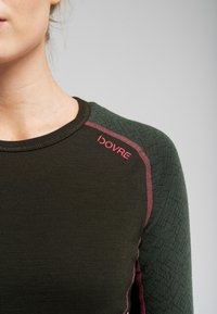 Langærmet skjorte i mørkegrøn med teksturerede skulderpaneler. Har rød syning og logo på venstre skulder. Blødt, tætsiddende design.