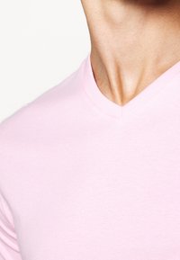 T-shirt rosa chiaro a V realizzato in morbido cotone, caratterizzato da un design semplice e una texture liscia, senza motivi o dettagli visibili.