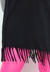 Sort frynset beklædning med en textureret overflade, parret med klare pink leggings. Bunden har lange, jævnt fordelte sorte frynser.