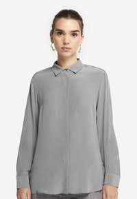 Helle graue Bluse mit langen Ärmeln und Kragen, glatter Textur und Knopfleiste. Verfügt über einen geraden Saum und Knopfbündchen.