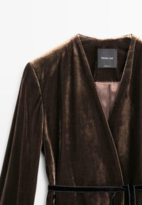 Fløjlbrun slå-om-kjole med lange ærmer, dyb V-hals og matchende bælte. Glat tekstur med let glans og blød foring synlig indeni.