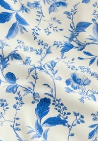 Tissu blanc avec des motifs floraux et feuillus bleus détaillés étalés sur la surface dans un design délicat.