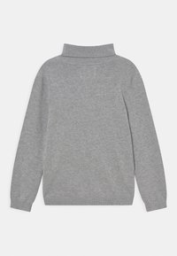 Jasnoszary, długi sweter z wełny z prążkowanym kołnierzem typu golf oraz prążkowanymi mankietami i dolnym wykończeniem, ułożony na płasko na białym tle.