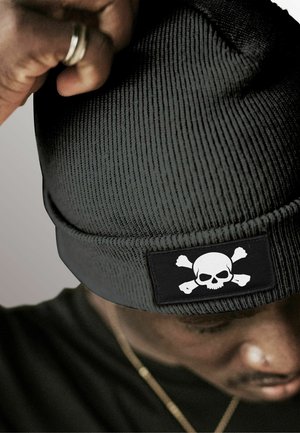 Black knitted beanie with ribbed texture features an embroidered skull and crossbones patch in white on a black background.