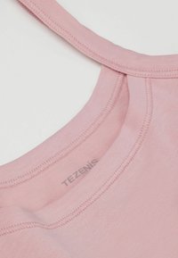 Světle růžový tílko s kulatým výstřihem, hladkou texturou a jemným prošíváním. Na zadní straně krku je vytištěné logo "TEZENIS".