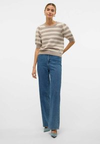 Pull rayé en tricot beige et crème, avec des manches courtes bouffantes. Associé à un jean bleu taille haute à jambes larges et des talons à bouts pointus.