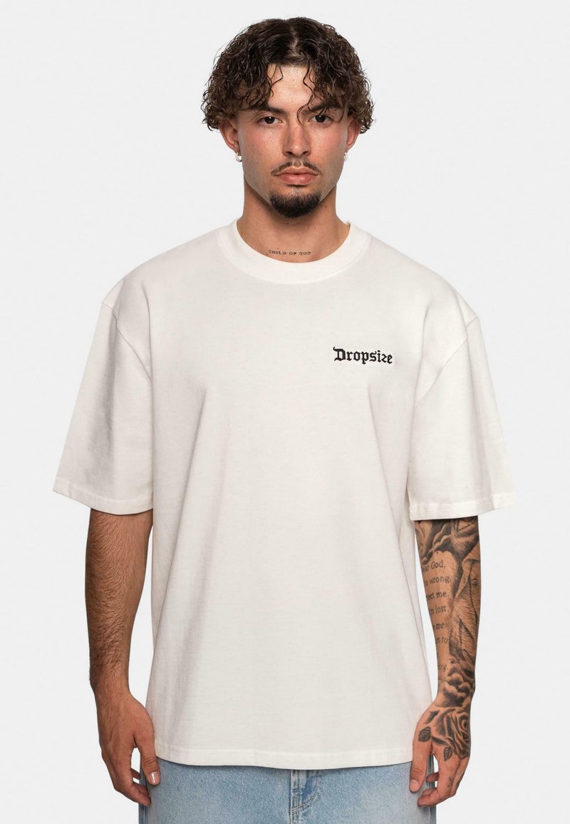 Tricou din bumbac de mari dimensiuni, de culoare crem, având un logo negru "Dropsize" pe partea stângă a pieptului. Mâneci scurte, guler rotund, croială lejeră.