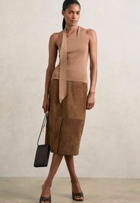 Top marrone senza maniche con dettaglio a fiocco, abbinato a una gonna midi in suede marrone. Una borsa nera e tacchi aperti completano il look.