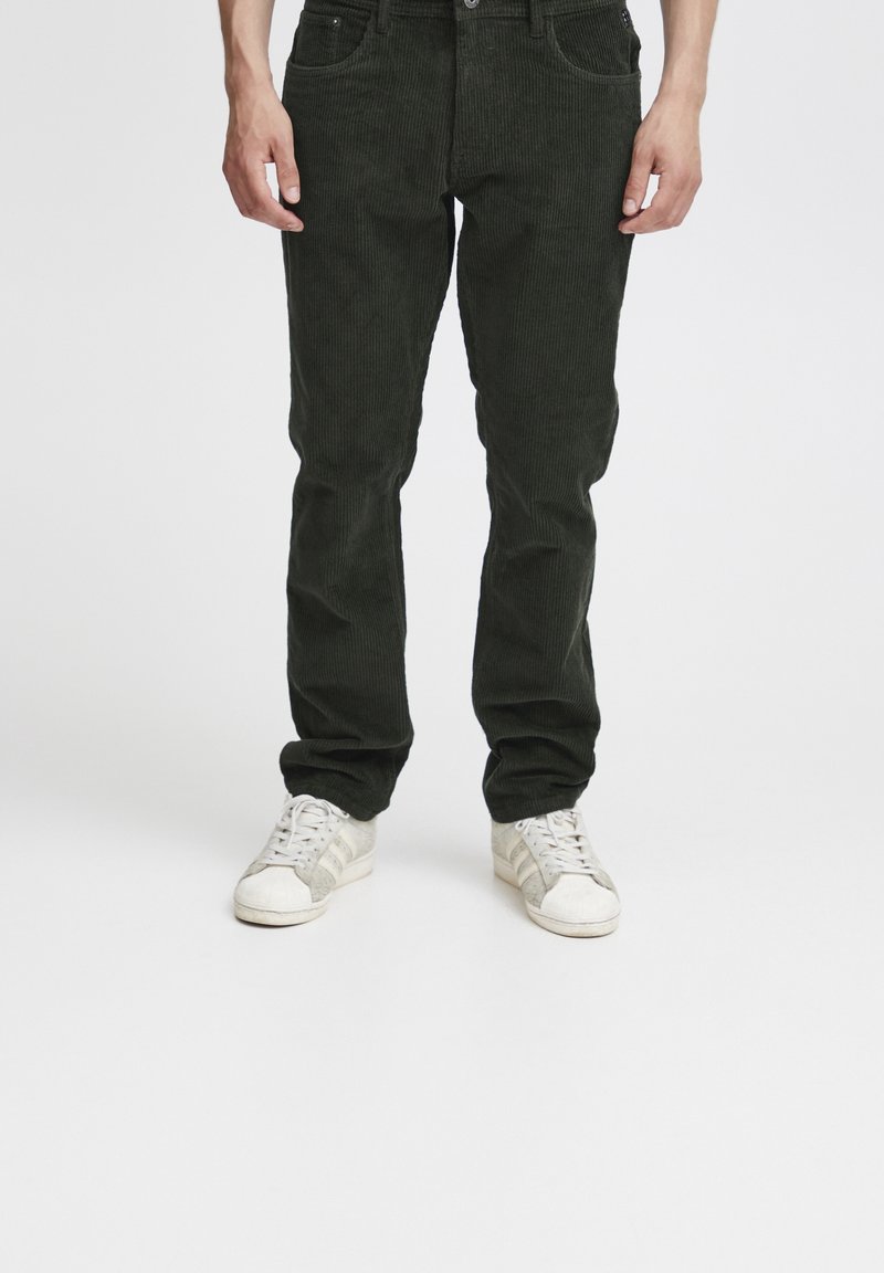 Donkergroene corduroy broek met een gestructureerde afwerking, vijf zakken en slim fit. Gecombineerd met witte sneakers met grijze accenten.