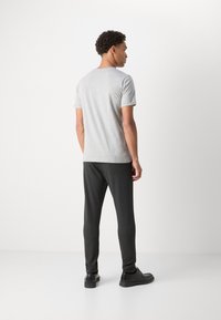 Camiseta gris de manga corta con cuello redondo, combinada con pantalones oscuros ajustados y zapatos negros, vista desde la parte trasera. Diseño sencillo, textura suave.