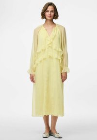 Vestido de gasa amarillo claro con capas con volantes, mangas largas y escote en V, que cuenta con un cierre de cuello con cordón y una silueta fluida.