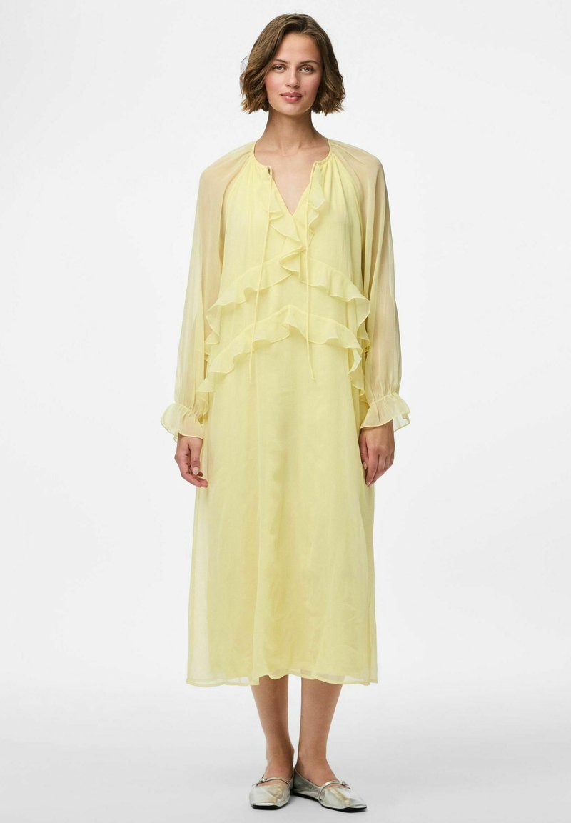 Vestido de gasa amarillo claro con capas con volantes, mangas largas y escote en V, que cuenta con un cierre de cuello con cordón y una silueta fluida.