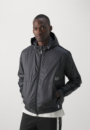 Giacca a vento nera in nylon con zip frontale, cappuccio regolabile, polsini elastici e dettagli con logo sul petto e sulle maniche.