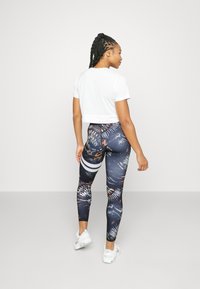 Afskåret hvid t-shirt parret med multifarvede, mønstrede leggings med blå, orange og sorte nuancer samt hvide vandrette striber.