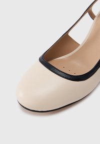 Μπεζ δερμάτινο παπούτσι με στρογγυλεμένη μύτη, μαύρες δερμάτινες λεπτομέρειες γύρω από το άνοιγμα και ομαλή υφή. Χωρίς ορατά μεταλλικά στοιχεία ή σχέδια.