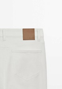 Jeans en denim blanc vue de dos montrant une poche arrière et un patch de marque en cuir marron sur la ceinture.