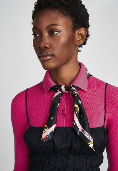 Suéter rosa ajustado em côr ribada com colarinho, por baixo de um vestido preto franzido. Um cachecol de estampa floral em preto com detalhes em rosa atado no pescoço.