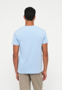 Ljusblå t-shirt med kort ärm i bomull, har rund halsringning och en slät yta, bärs tillsammans med ljusbeige byxor.