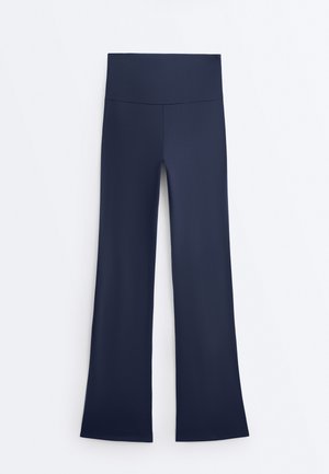 Pantaloni de yoga bleumarin cu talie înaltă, cu o bandă lată în talie și picioare evazate, așezați pe o suprafață plată pe un fundal alb.