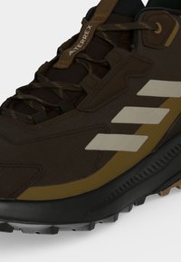 Gros plan sur une chaussure de randonnée Adidas Terrex marron avec des bandes beige, des lacets texturés et une semelle noire robuste pour une utilisation en extérieur.