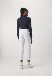Haut à manches longues marine avec un col, associé à un pantalon court blanc avec des poches arrière. Des chaussures de sport à lacets complètent la tenue.