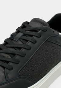 Zwarte leren sneaker met een textuurdesign, ronde neus, vetersluiting en een witte rubberen zool. Heeft een reliëflogo-detail op het zijpaneel.