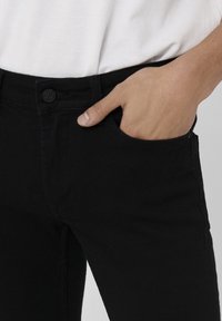 Jeans negros fabricados con una mezcla de algodón, que presentan un cierre de botón, bolsillos frontales y un diseño ajustado. Textura suave, con un ligero estiramiento.