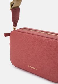 Torba na ramię z teksturowanej skóry w głębokim różu z złotym zamkiem i okuciami. Regulowany pleciony pasek, prostokątny kształt, minimalne oznakowanie.