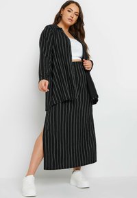 Completo a righe bianche e nere composto da una gonna lunga e aderente e una camicia con bottoni e colletto. Indossato con scarpe da ginnastica bianche.