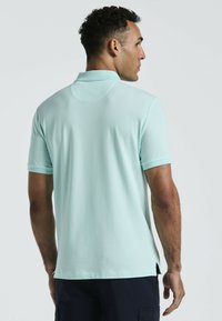 Licht mintgroene polo met korte mouwen, kraag en een zijsplit aan de onderkant. De stof lijkt glad en ademend, geschikt voor casual dragen.