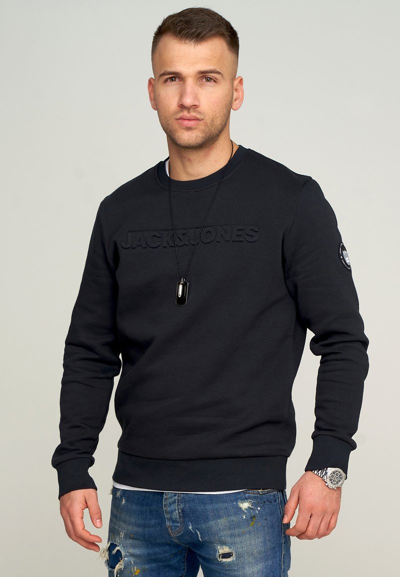 Schwarzer Sweatshirt mit eingeprägtem "JACK & JONES" Logo. Verfügt über einen Rundhalsausschnitt, lange Ärmel und gerippte Säume. Wird mit ausgebleichten blauen Jeans getragen.
