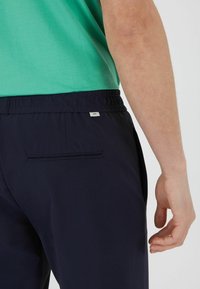 Marinen bløde badshorts med elastisk talje, baglomme og et lille logo. Materialet virker glat og let.