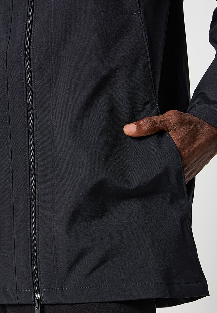 Veste noire imperméable avec une texture lisse, dotée d'une fermeture éclair avant, de poches latérales et d'une coupe légèrement ample près de l'ourlet.