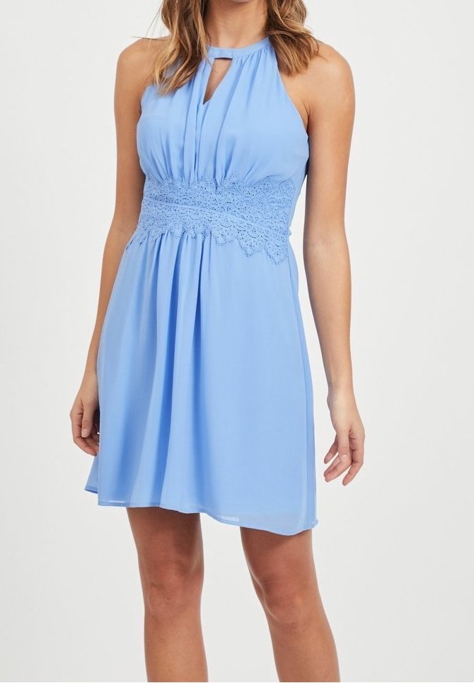 Robe bleu clair sans manches avec col licou, détail œillet et large ceinture en dentelle, tombant au-dessus des genoux sur une femme debout.