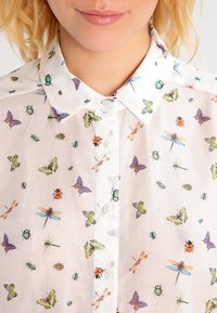 Camicia bianca con colletto, caratterizzata da un motivo di insetti colorati, comprese farfalle e coleotteri, su un tessuto leggero.