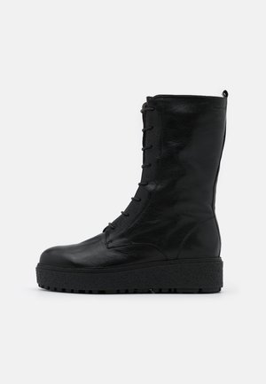 Bottine en cuir noir avec lacets, surface texturée, bout rond et semelle épaisse contrastante pour plus de hauteur et d'adhérence.